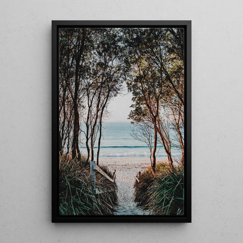 Framed artwork of a beach scene with trees and ocean view on a white wall.