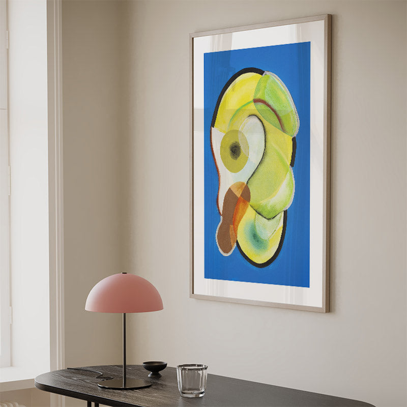 Framed artwork of a colorful parrot on a wall above a table with a lamp and glass.