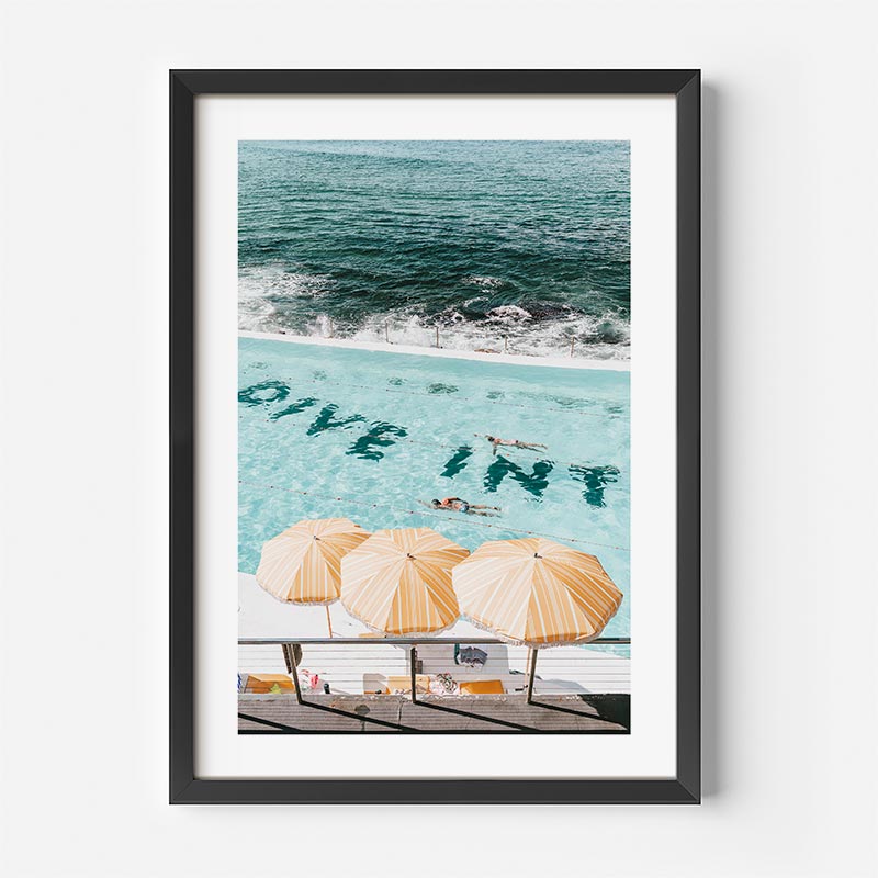 Framed artwork of a pool with 'Dive In' text and umbrellas, featuring a beach and ocean view.