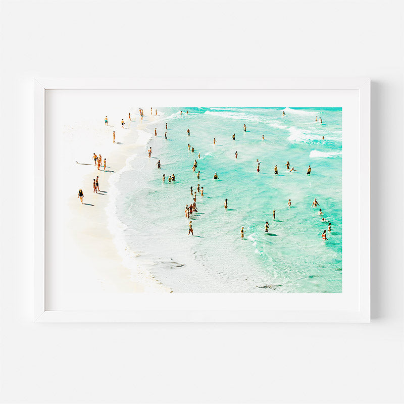 Framed artwork of a beach scene with people in the water and on the sand.