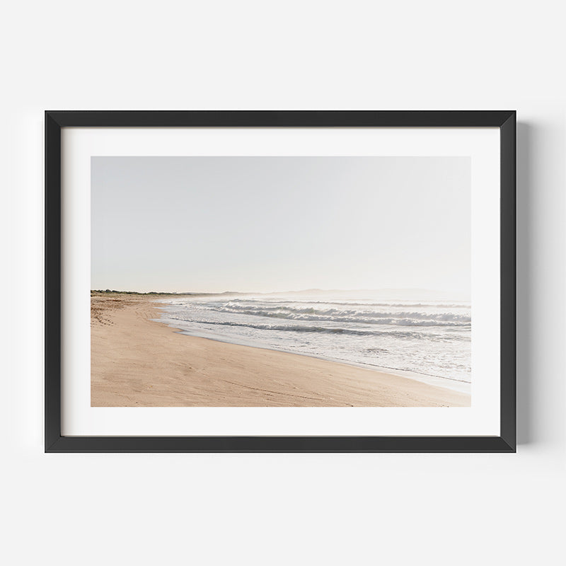 Framed artwork of a beach scene with water and sand on a white wall