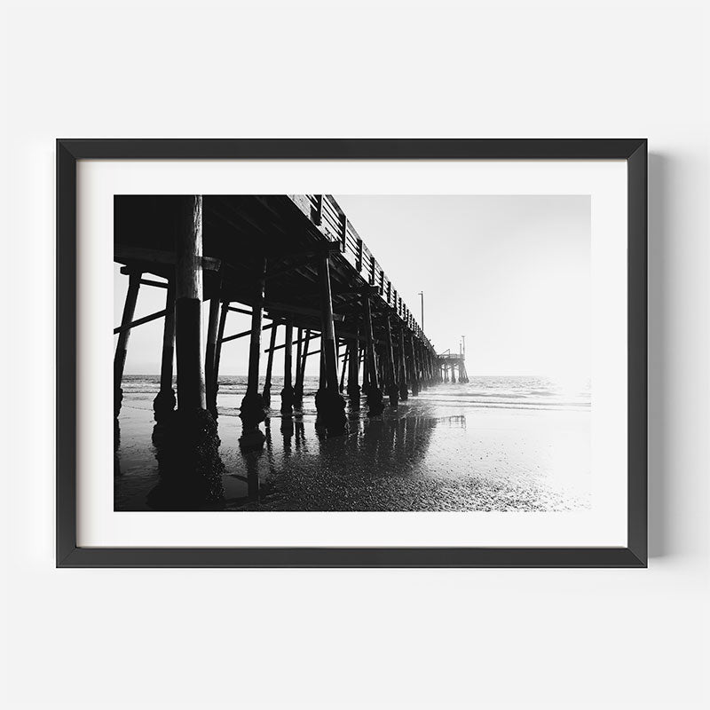 Framed black and white photograph of a pier on a beach