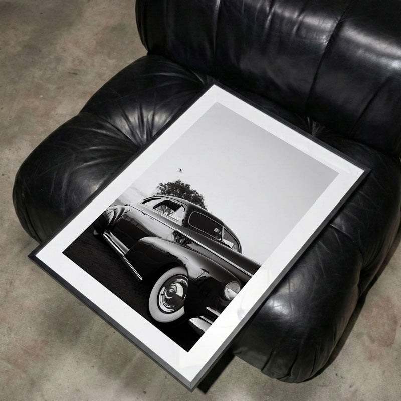 Framed black and white photo of a classic car on a black leather armchair.