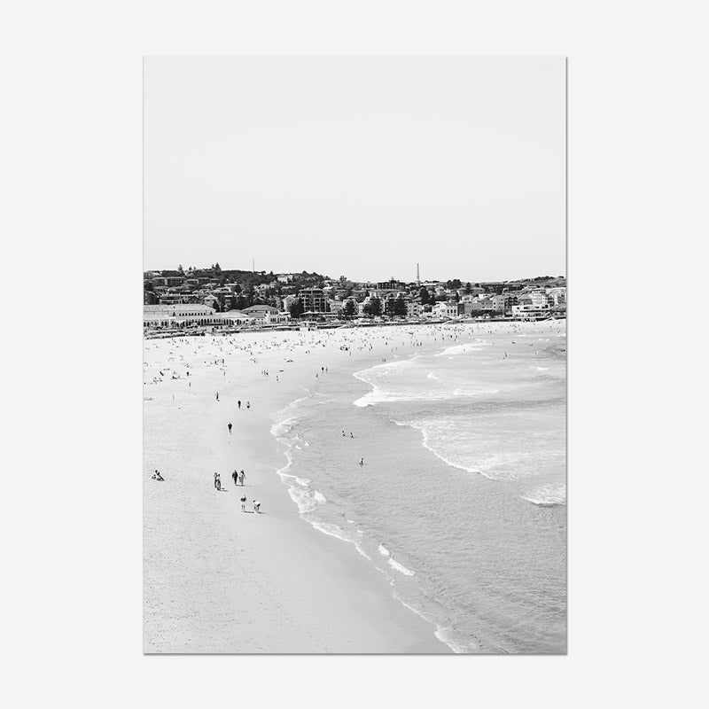 Black and white photo of a beach with people and a cityscape in the distance.