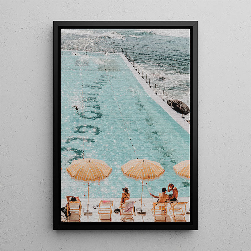 Framed photograph of a pool with people under umbrellas and ocean view.