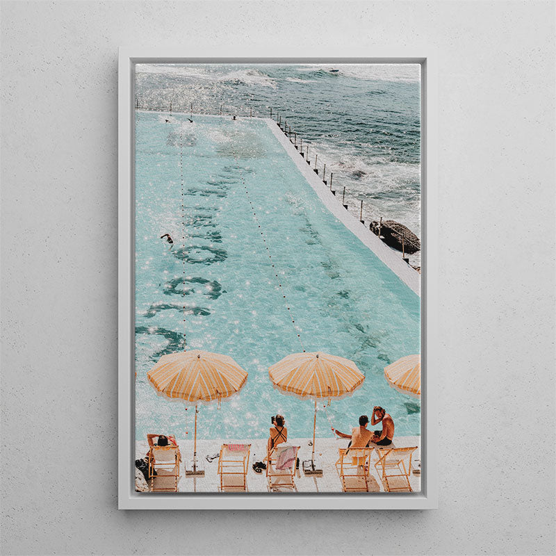 Framed artwork of people by a pool with umbrellas on a gray wall.
