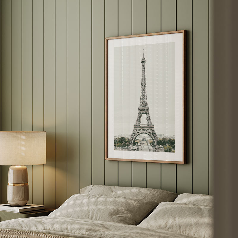 Framed picture of the Eiffel Tower on a green paneled wall above a bed.