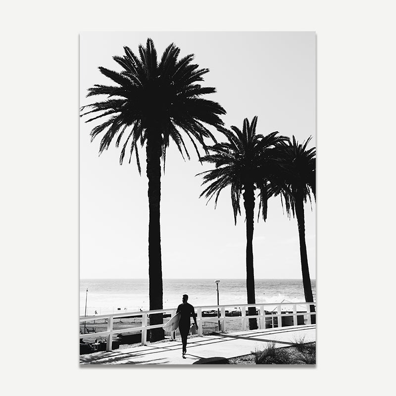 Black and white silhouette of a person walking along a boardwalk with palm trees and ocean in the background.
