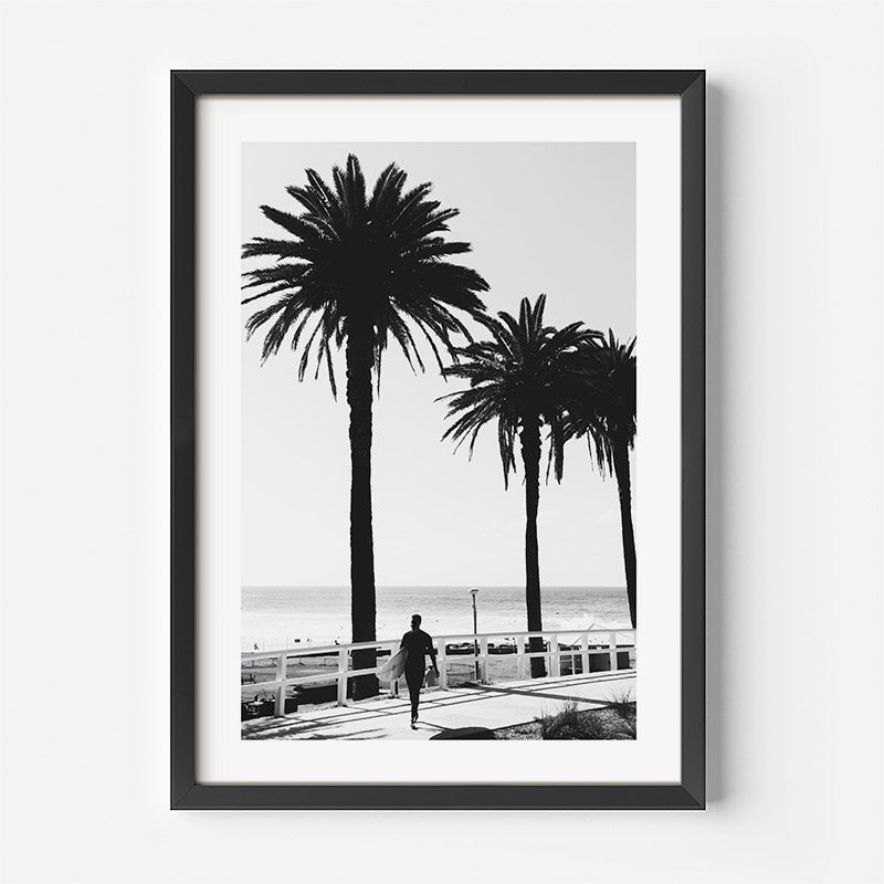 Framed black and white print of a person walking along a promenade with palm trees.