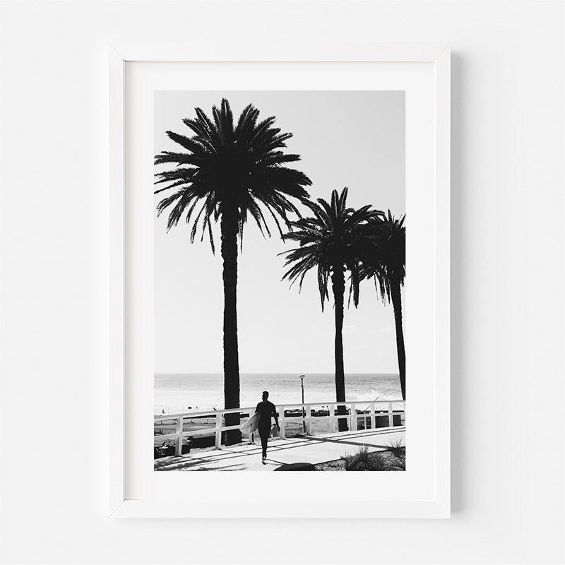 Framed black and white print of a beach scene with palm trees and a person walking.