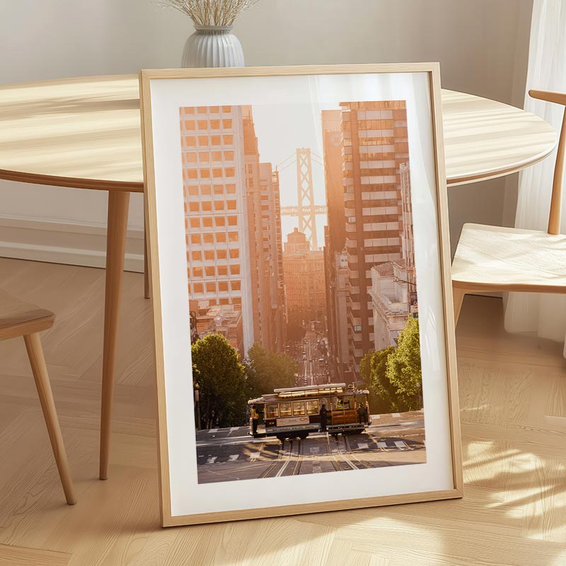 Framed cityscape print on a wooden table with a chair and vase in the background