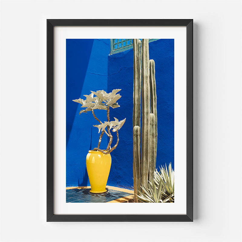 Framed photograph of a yellow vase with plants against a blue wall