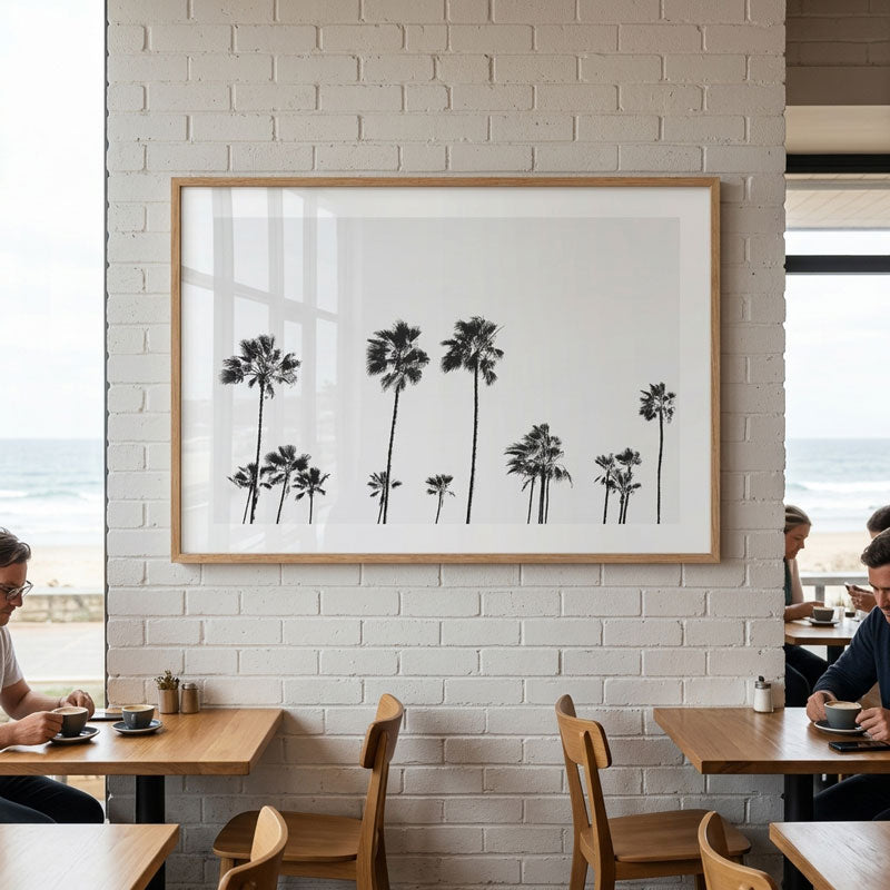 Framed artwork of palm trees on a white brick wall in a restaurant setting.