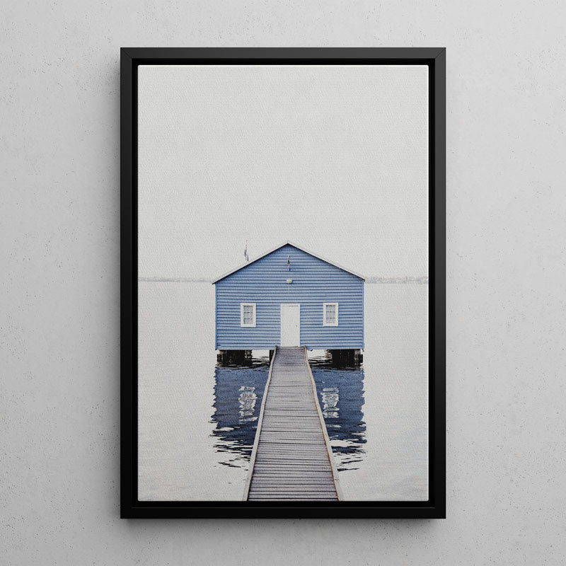 Framed artwork of a blue house on a dock with a white wall background