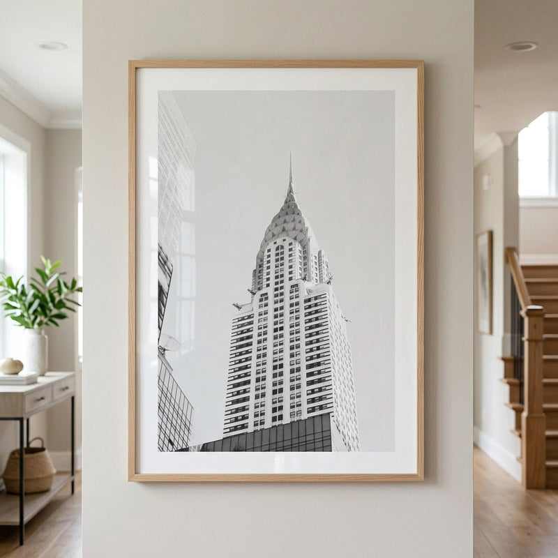 A framed black and white architectural art print of the Chrysler Building hanging on a light beige wall in a modern, sunlit hallway.