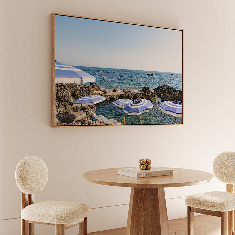 Framed artwork of a beach scene above a dining table with chairs.