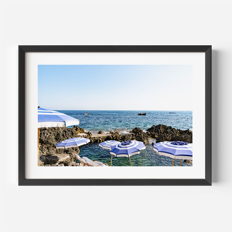 Framed photograph of beach umbrellas by the ocean with a black frame.