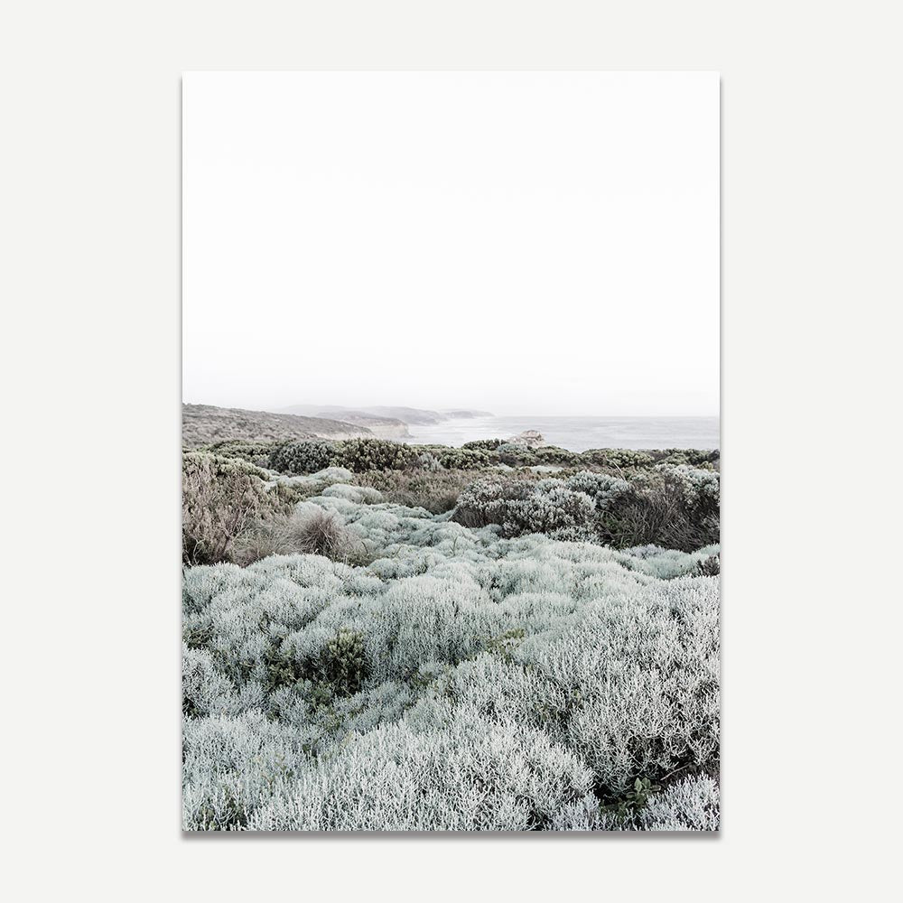 A framed art print featuring a coastal landscape with shrubbery and a misty background, in a sage green color palette.