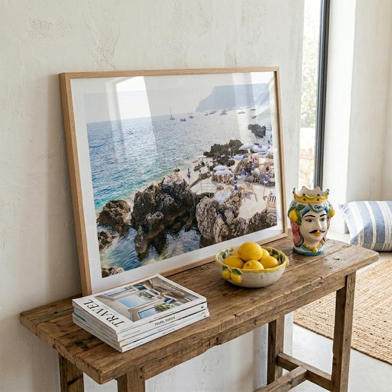 Framed photograph of a coastal scene on a wooden console table with books and a bowl of lemons.