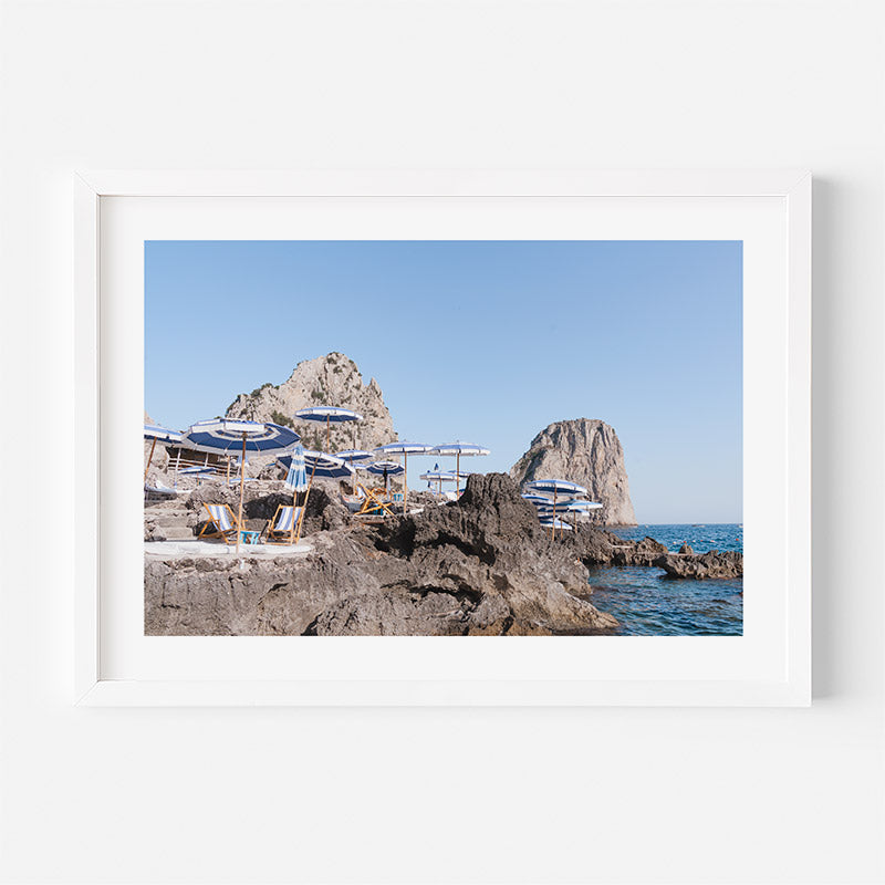 Beach scene with lounge chairs and umbrellas on rocky cliffs overlooking the ocean.