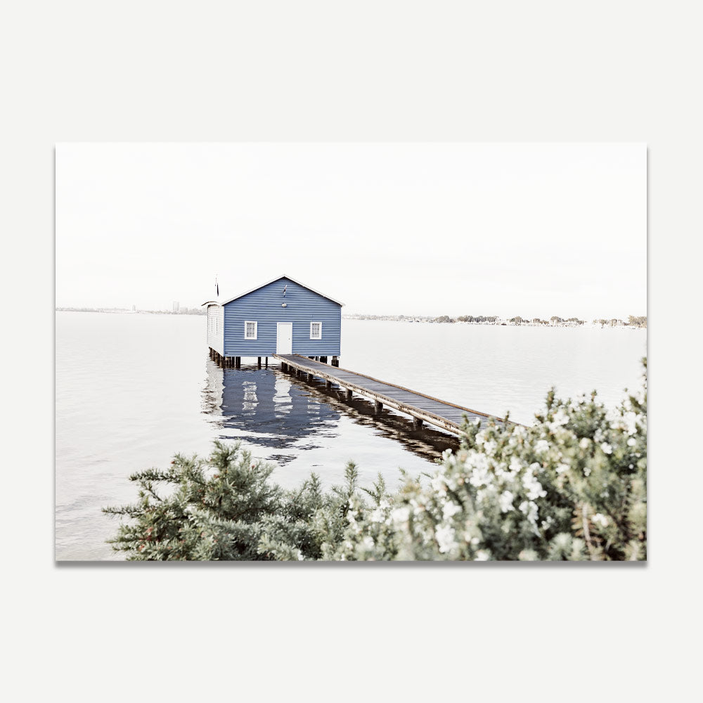 Art print of the Crawley Edge Boatshed, featuring a small blue boat house at the end of a jetty, with calm water and reflections.