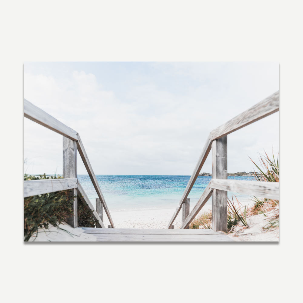A wall art print featuring white-washed stairways leading down to a pristine beach with blue waters and a clear sky.