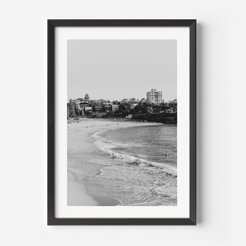 Framed black and white beach scene with buildings in the distance.