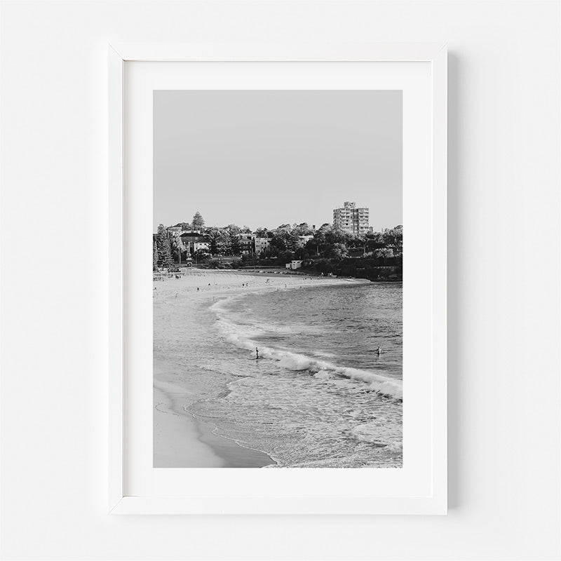 Framed black and white beach scene with buildings in the distance.