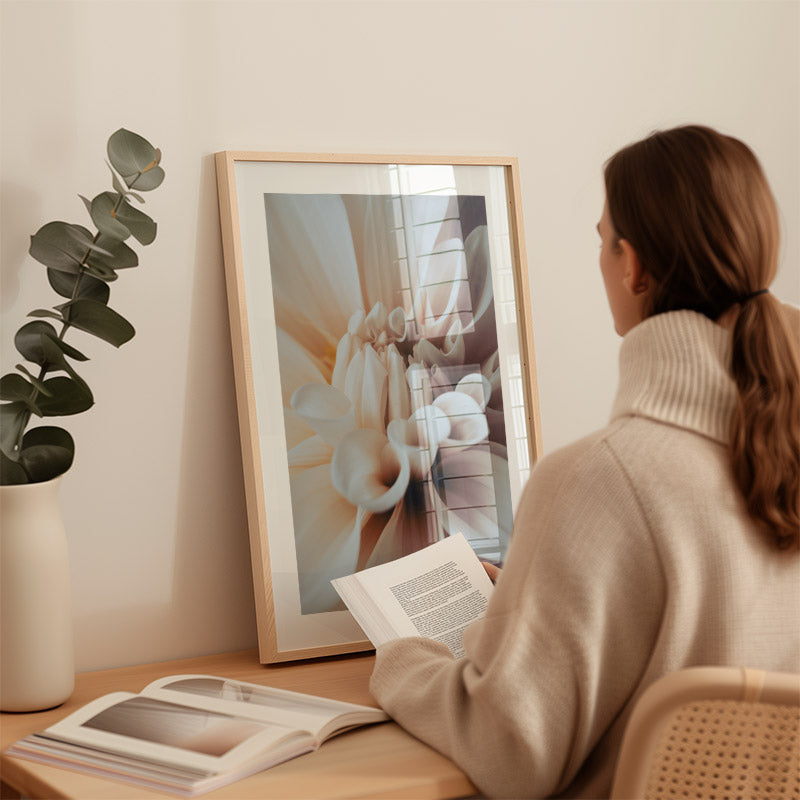 Woman reading a book next to a framed artwork in a cozy room.