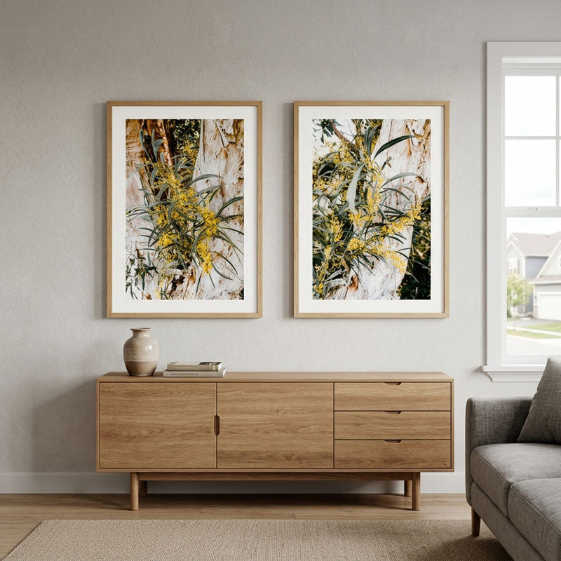 Two framed botanical art prints with yellow flowers hang on a light gray wall above a wooden sideboard in a modern living room setting.