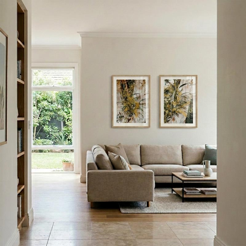 A modern living room featuring a beige sectional sofa, a wooden coffee table, and two framed botanical art prints hanging on the wall above the sofa.