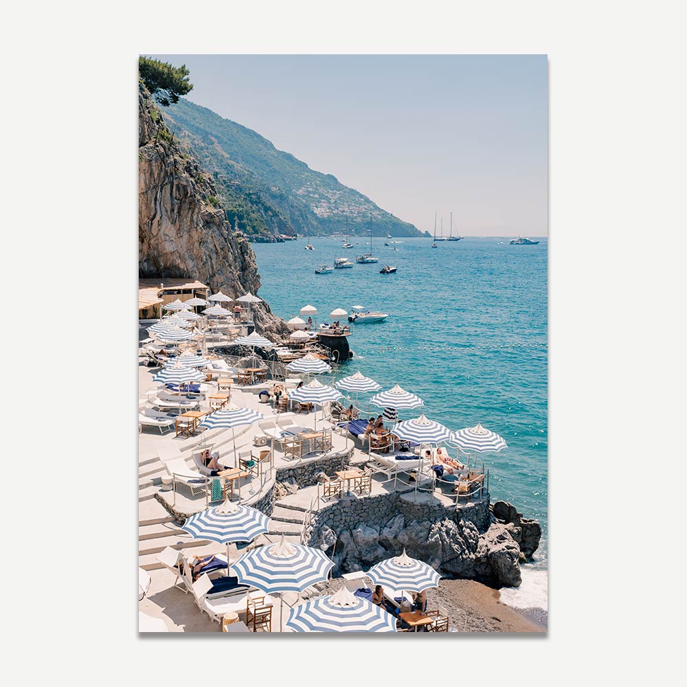 Exclusive photograph of Music on the Rock beach club on the Amalfi Coast, featuring blue and white beach umbrellas, azure waters, and a scene of luxury and relaxation. Perfect for adding a touch of Italian summer to any space.