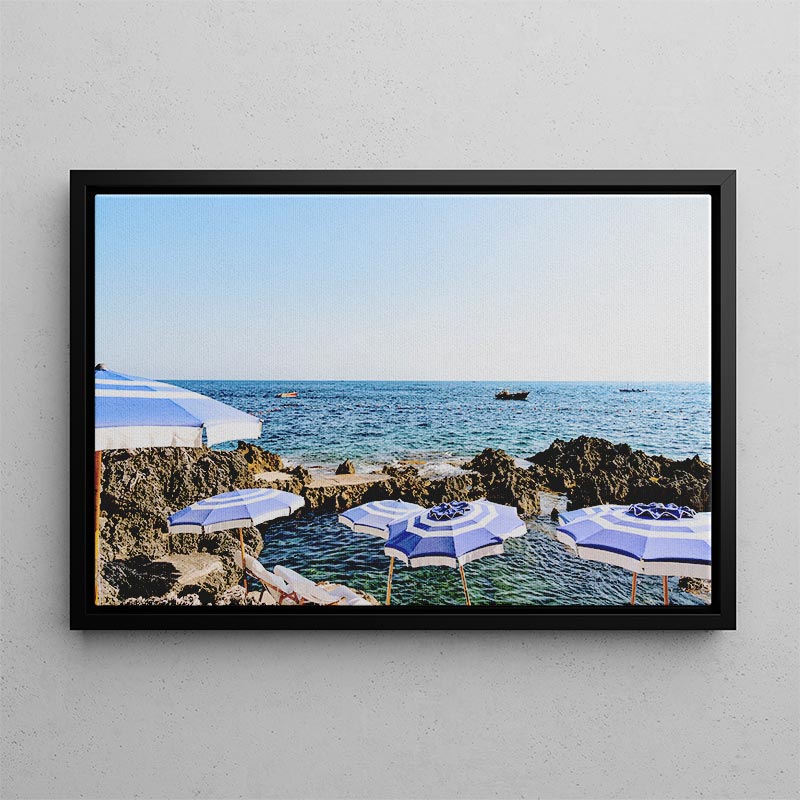 Framed photograph of beach umbrellas by the ocean on a gray wall.