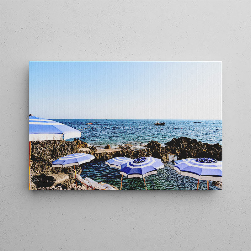 Canvas print of blue and white umbrellas by the ocean on a gray wall.