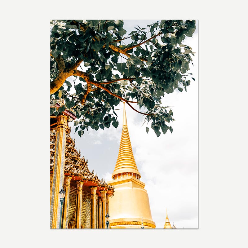 A vertical photographic print of a golden temple stupa framed by green tree leaves and ornate columns, shown against a light gray background.