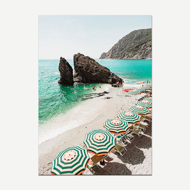 Beach scene with green and white umbrellas, clear blue water, and rocky outcrops.