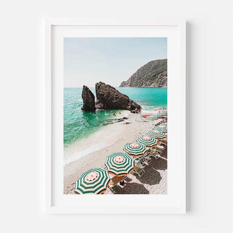 Framed photograph of a beach with green and white striped umbrellas and rocky outcrops.