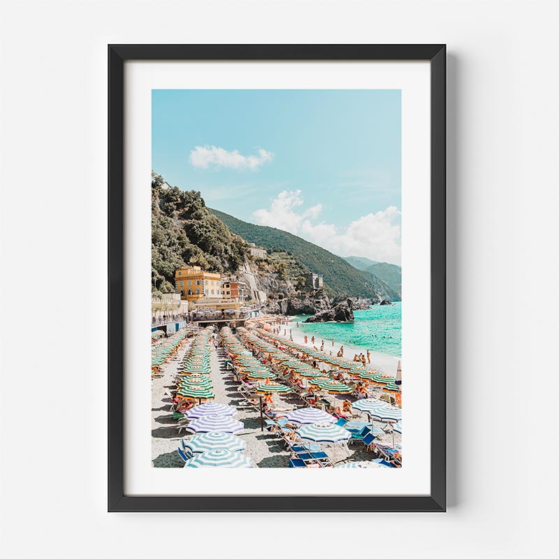 Framed photograph of a beach scene with chairs and umbrellas, mountainous background.