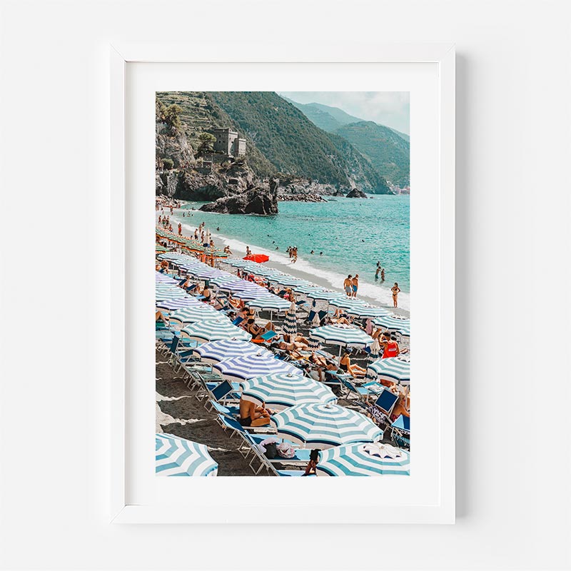 Framed photograph of a beach scene with people, umbrellas, and mountains.