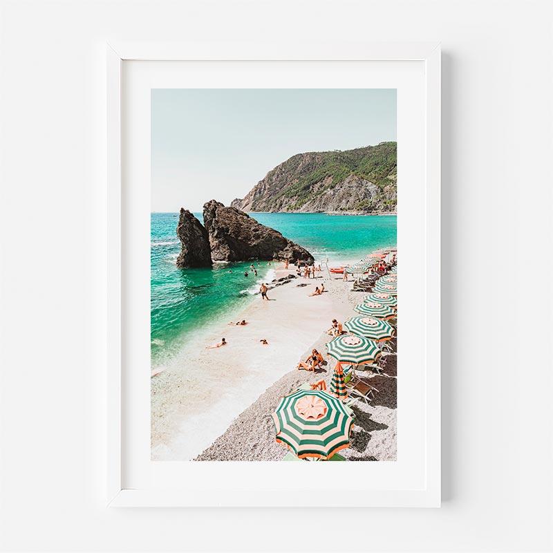 Framed photograph of a beach scene with people, umbrellas, and rocky cliffs.