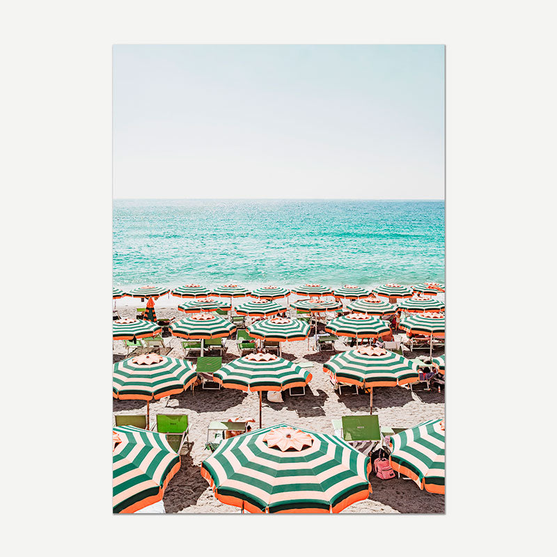 Beach scene with green and white striped umbrellas and chairs on a sandy beach.