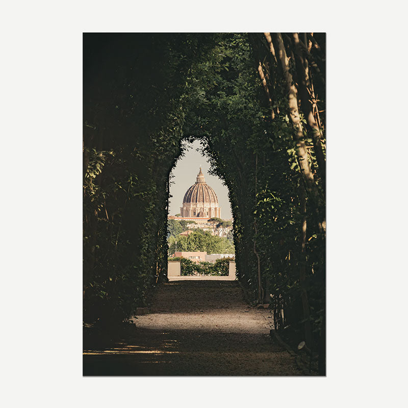 A vertical photographic art print depicting a scenic view of the Vatican's dome of St. Peter framed by a dark, leafy archway in Rome, shown against a light gray background.