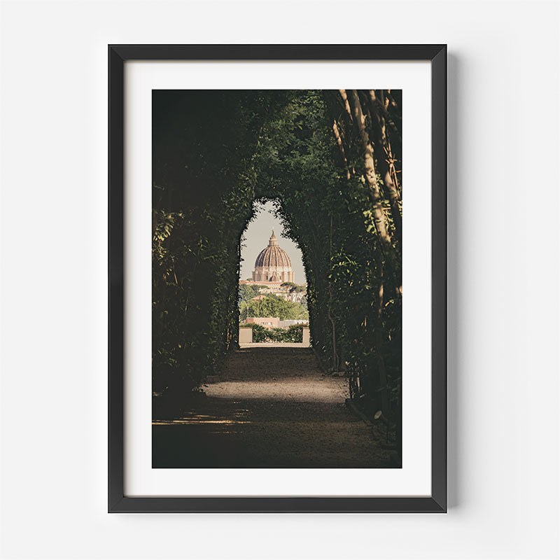 A framed art print featuring a scenic photograph of a domed cathedral seen through a dark, tree-lined path, presented in a black frame with a white mat against a light gray background.
