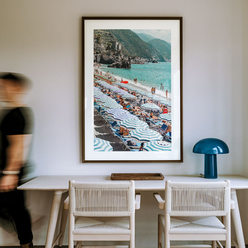 Framed photograph of a beach scene on a wall above a dining table with chairs.
