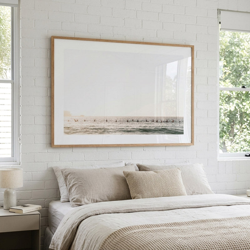 Neatly made bed with beige bedding in a room with a large framed picture on the wall.