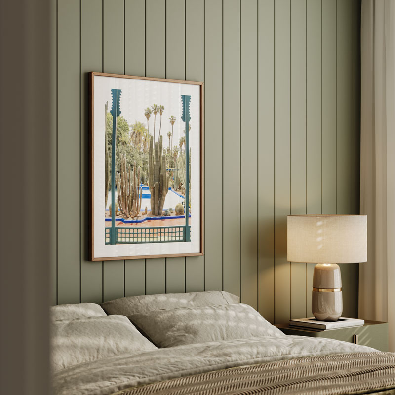 Framed artwork above a bed with a lamp on a nightstand against a striped wall.