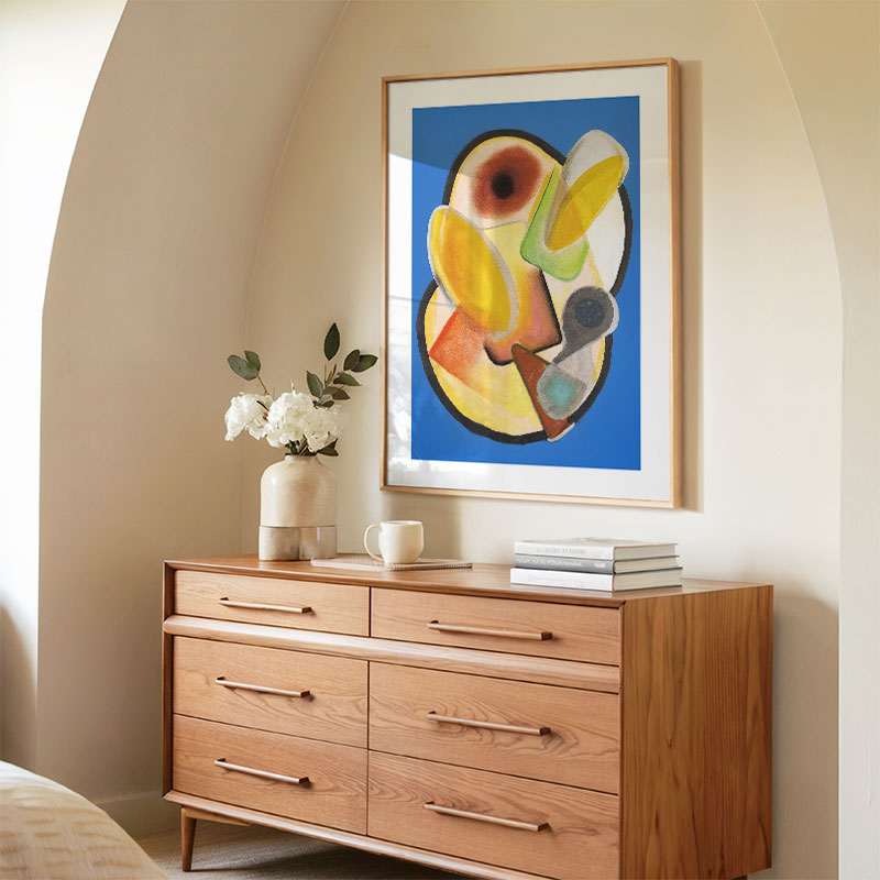 Wooden dresser with a vase of flowers and books, framed abstract art on the wall.