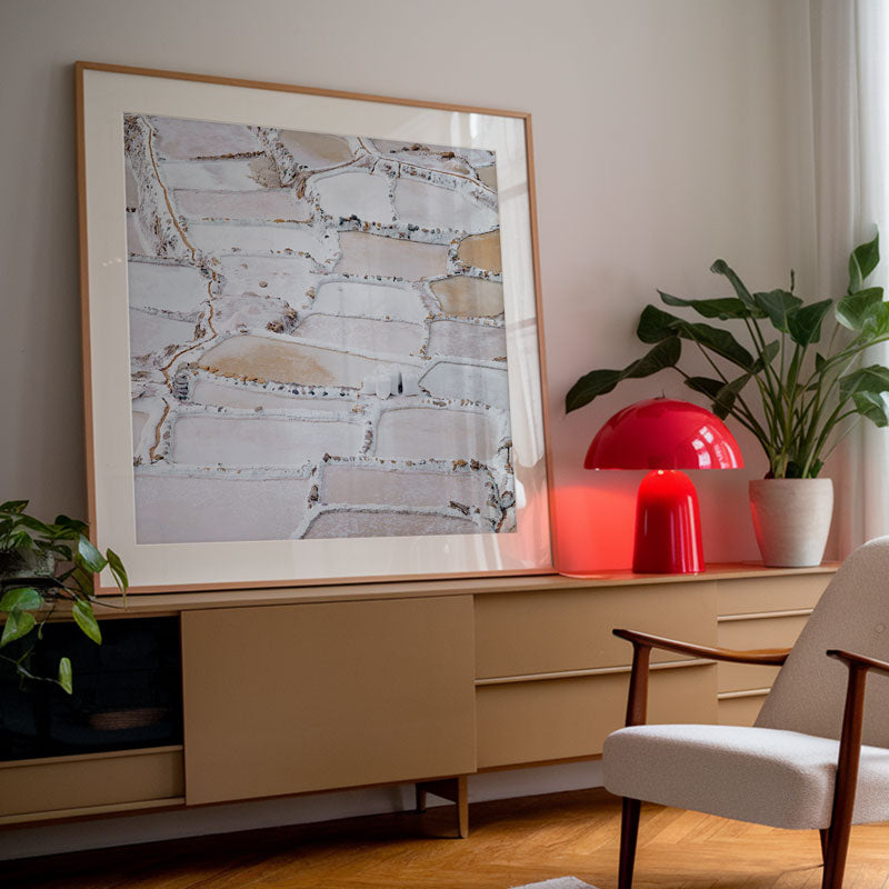 Modern interior with a framed abstract artwork, red lamp, and plant on a wooden cabinet.