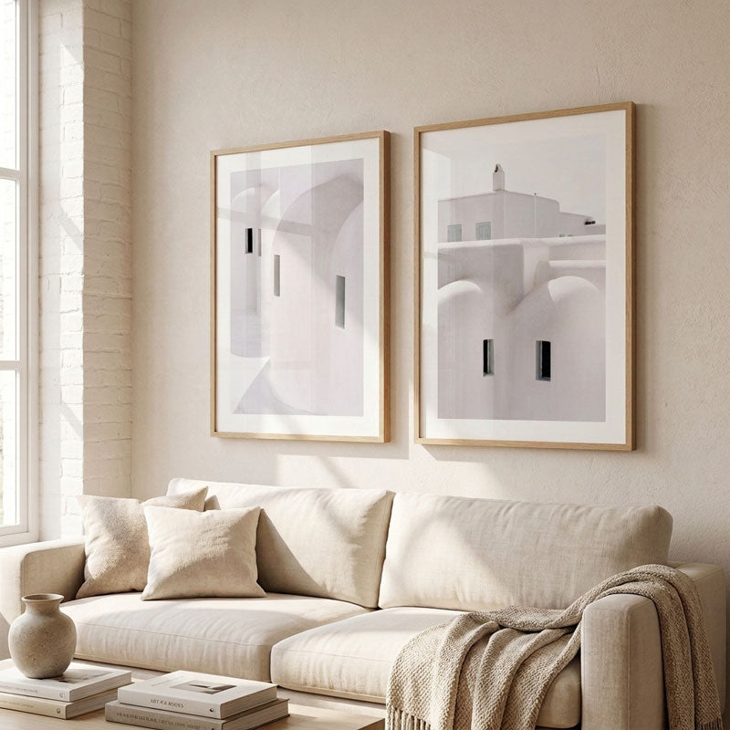 Two minimalist framed art prints with light wood frames hang on a beige wall above a cream-colored sofa in a bright, modern living room.