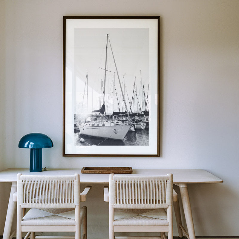 Framed black and white photograph of boats on a wall above a dining table with chairs.